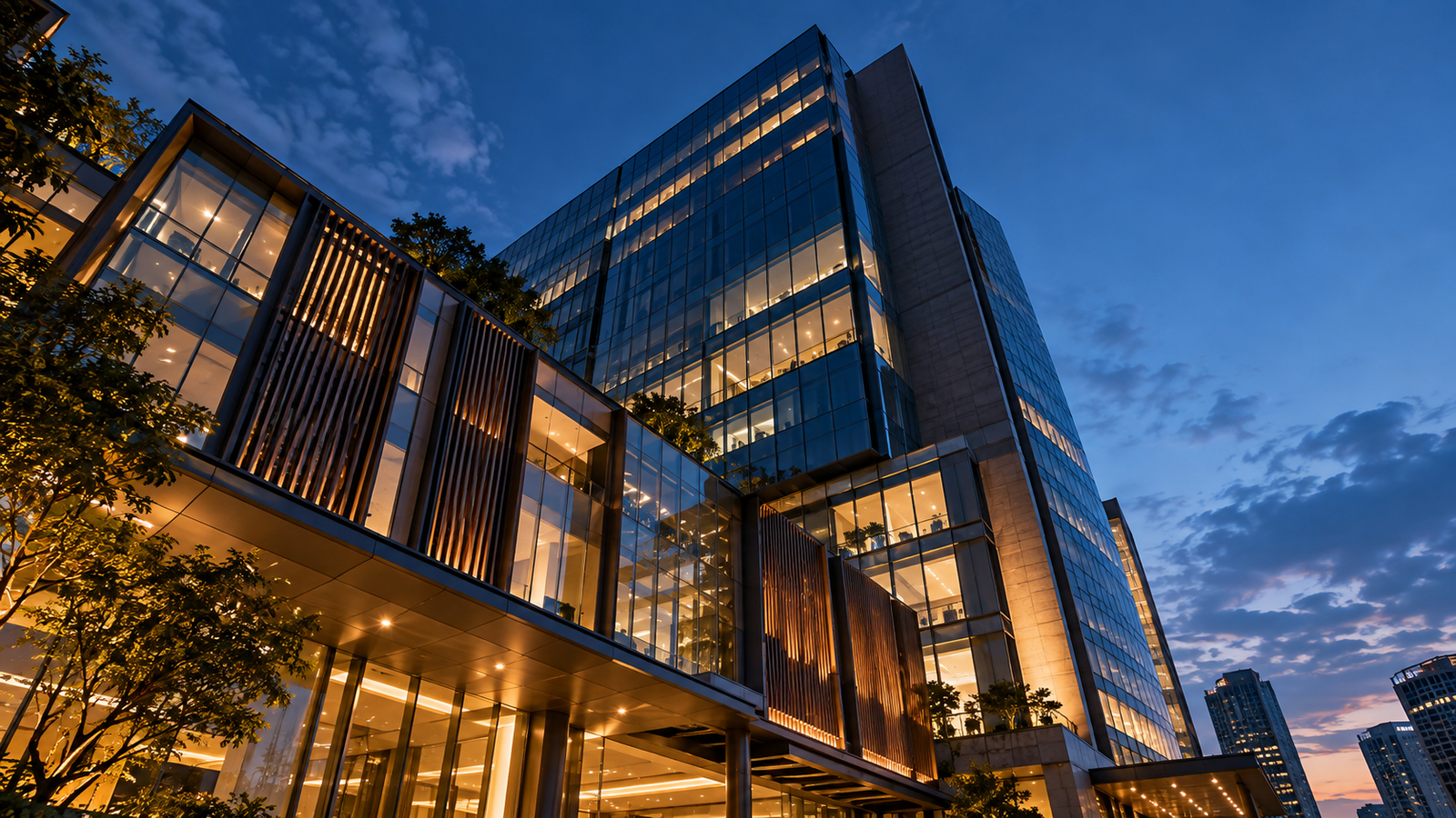 Gedung perkantoran modern dengan fasad kaca yang menyala di senja hari